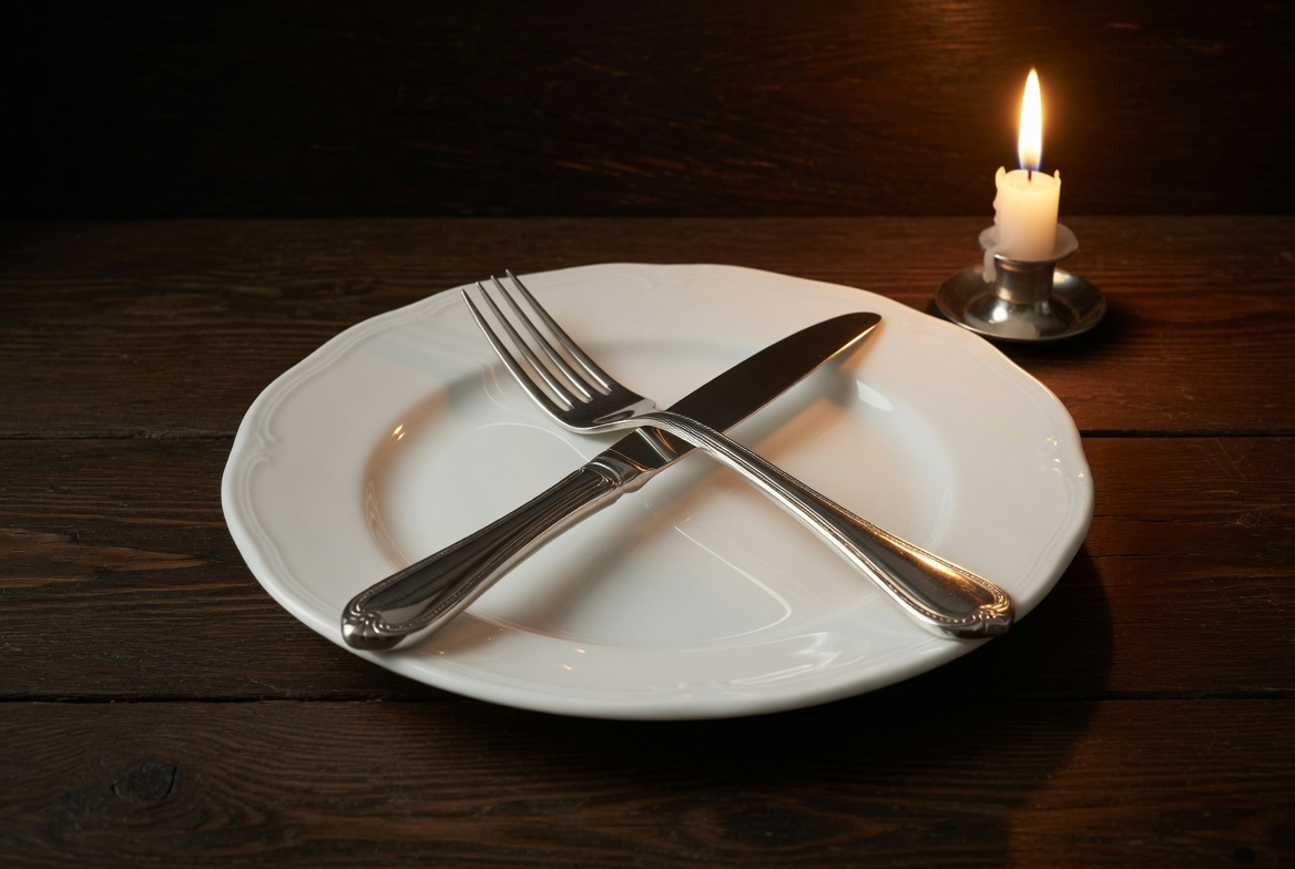 Empty plate with crossed fork and knife on dark table