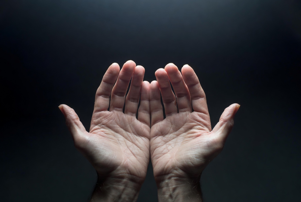 Empty open hands palms up against dark background
